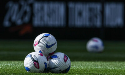 A stack of three NWSL game balls sitting on the pitch.