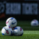 A stack of three NWSL game balls sitting on the pitch.